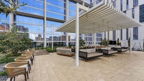 Een modern buitenzitgedeelte met rieten stoelen en banken, een pergola en een uitzicht op de skyline door grote ramen.