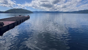 Un lac paisible avec une jetée qui s’avance sur l’eau, entouré de montagnes et surplombé d’un ciel partiellement nuageux.