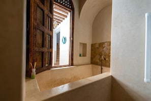 Un baño con bañera, una puerta de madera decorativa y una pared de piedra.