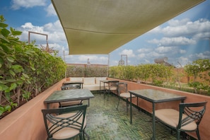 An outdoor patio with tables and chairs, a cushioned seating area, and a view of the sky. - Riad Nalan & Spa (Marrakech)