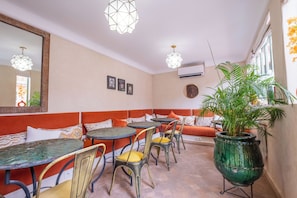 A dining area with a long bench, multiple tables, chairs, and hanging pendant lights. - Riad Nalan & Spa (Marrakech)