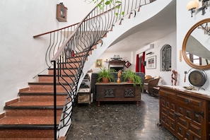 A staircase with a metal railing, a wooden cabinet with plants, and a mirror on the wall.
