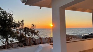 A coastal view with a sunset, a car parked on the right, and a white building structure.
