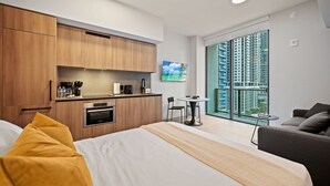 A modern hotel room with a bed, a small kitchenette, a dining area, and a large window with a city view. - Stylish Studio Steps from Brightline & Downtown (Miami)