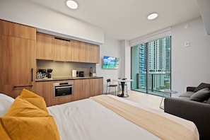 A modern hotel room with a bed, a small kitchenette, a dining area, and a large window with a city view. - Stylish Studio Steps from Brightline & Downtown (Miami)