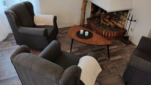 A cozy living room with a fireplace, two armchairs, a coffee table, and a rustic brick fireplace surround. - Ekängen Garde (Ljugarn)