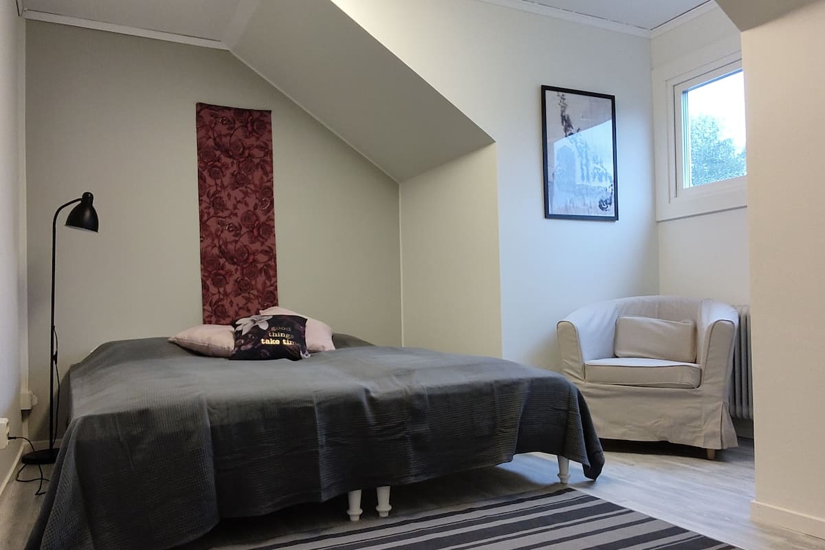 A bedroom with a bed, a chair, a lamp, a window, and a framed picture on the wall.