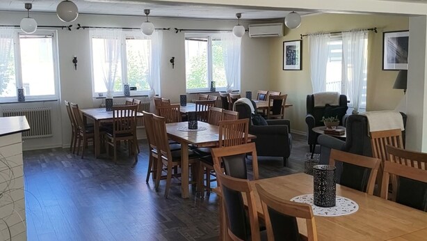 A spacious dining area with wooden tables and chairs, a sofa, and a television. - Ekängen Garde (Ljugarn)