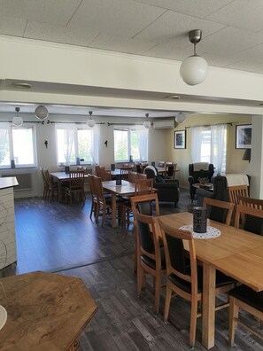 A spacious dining area with wooden tables and chairs, a sofa, and a television. - Ekängen Garde (Ljugarn)
