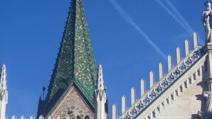 Un edificio con techo verde a dos aguas, un reloj y una estatua a la derecha.