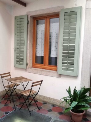 Un piccolo patio con tavolo e sedie, una finestra con persiane e una pianta in vaso.