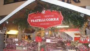 Un puesto de mercado con varios tipos de carne y un cartel que dice 'Salumi Trentini Fratelli Corra'.