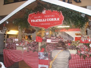 Un banco di mercato con diversi salumi e un cartello con su scritto 'Salumi Trentini Fratelli Corra'.