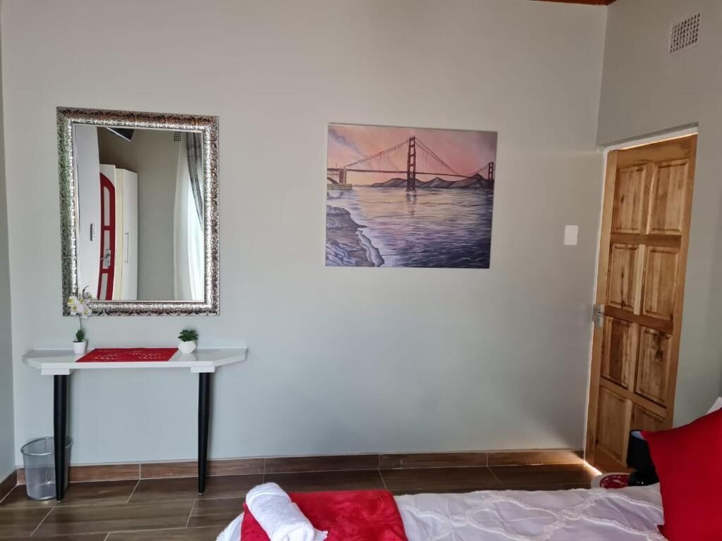Un dormitorio con cama, mesita de noche, espejo, un cuadro de un puente y una puerta de madera.
