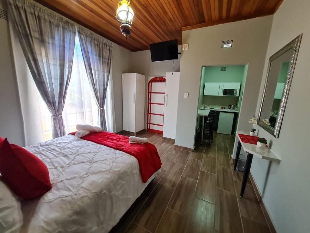 Camera da letto con un letto, tende, soffitto in legno, televisore, angolo cottura e uno specchio.