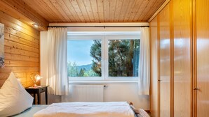 A bedroom with two beds, a window with curtains, a radiator, and wooden walls. - Cozy Apartment with Private Sauna, Garden, and Sunny Terrace (Feldberg)