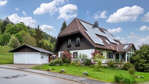 A house with a sloped roof, solar panels, a garage, and a well-maintained lawn. - Cozy Apartment with Private Sauna, Garden, and Sunny Terrace (Feldberg)