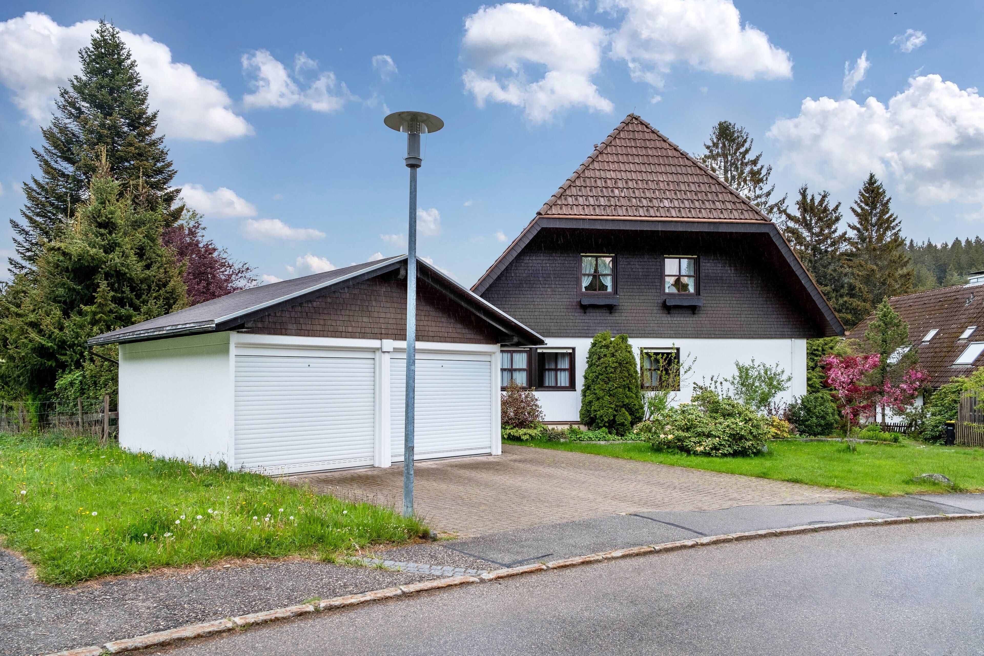 Ein zweistöckiges Haus mit Garage, geneigtem Dach und gepflegtem Garten.