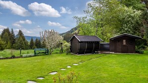 A green lawn with stepping stones, a wooden shed, a bench, and a tree with blossoms. - Cozy Apartment with Private Sauna, Garden, and Sunny Terrace (Feldberg)