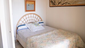 Un dormitorio con cama, cabecera, lámpara de pared e imagen enmarco.