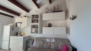 Un espacio habitable compacto con kitchenette, estanterías empotradas, un sofá estampado y un ventilador de techo.