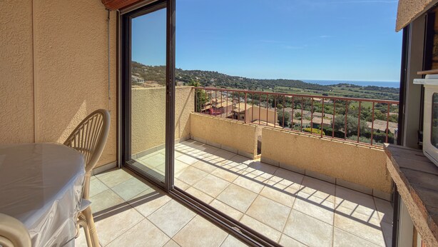 Un balcón con vistas al mar y las colinas, una silla y una mesa.