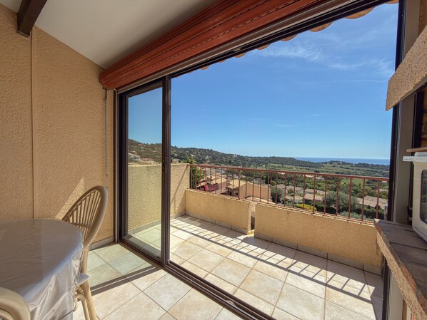 Ein Balkon mit Blick auf Meer und Hügel, ein Stuhl und ein Tisch.