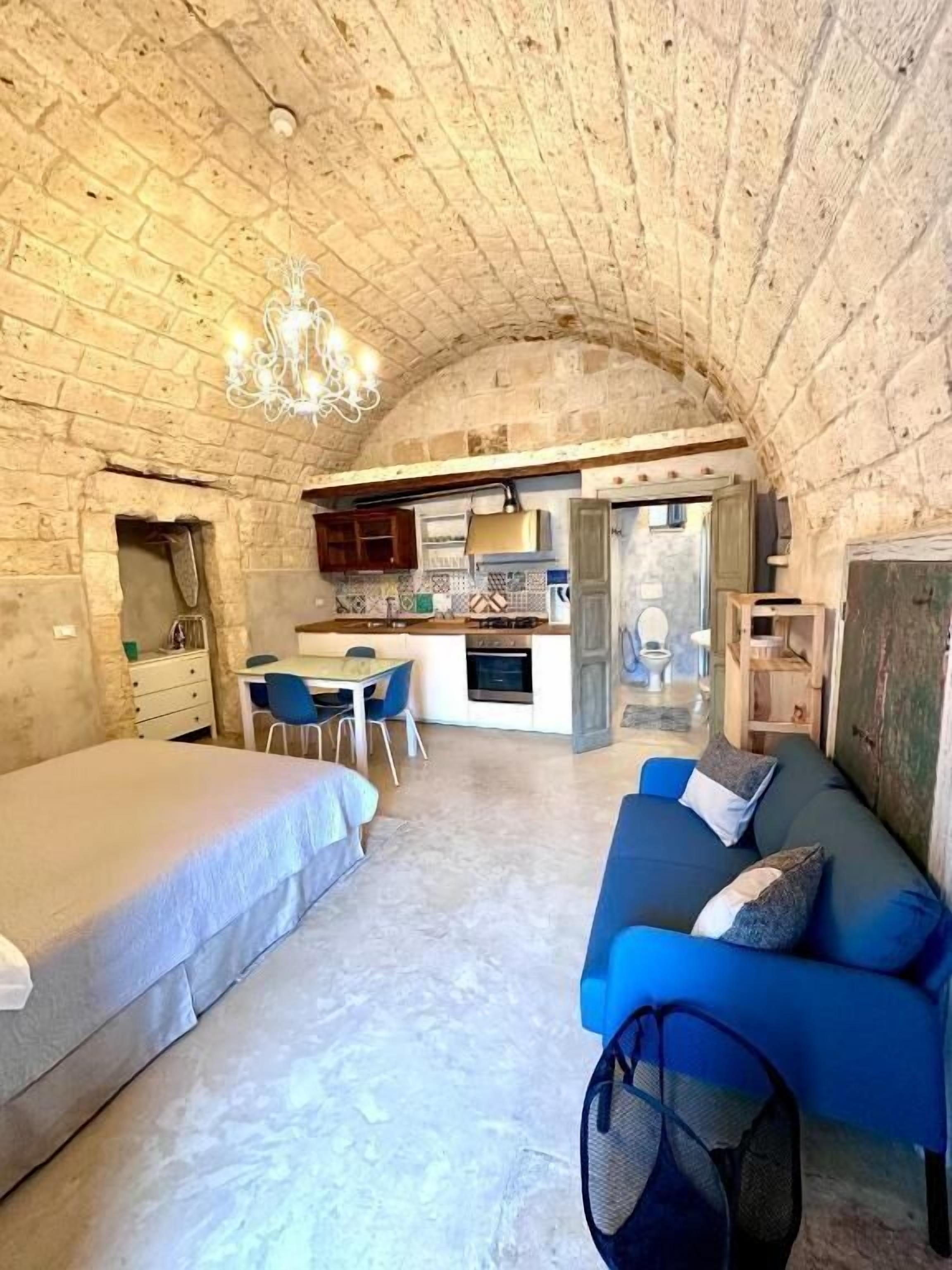 Quarto rústico com uma cama, um sofá azul, área de jantar e cozinha.