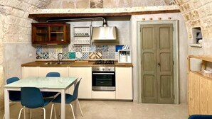 A compact kitchen with a built-in oven, a dining table with chairs, and a green door. - DIMORA DI LEO (Bisceglie)