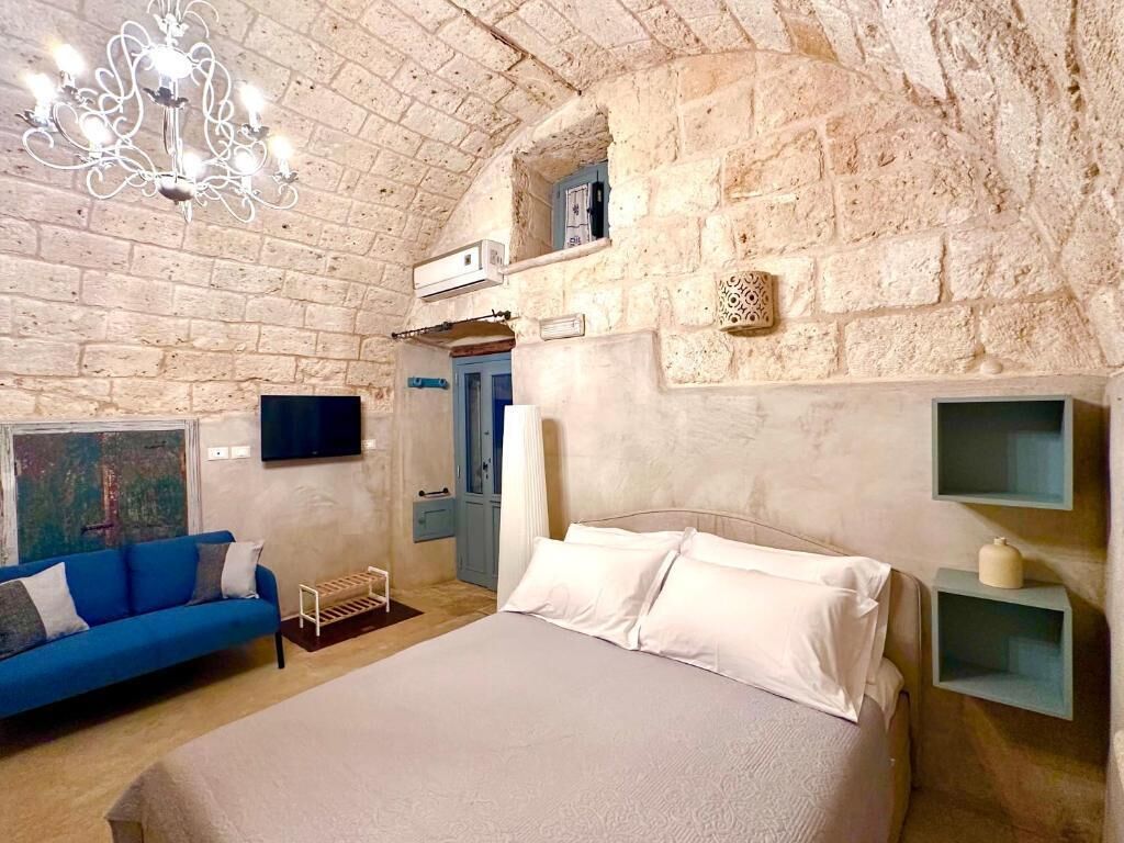 A bedroom with a stone wall, a bed, a blue sofa, a TV, and a chandelier.