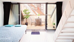 A bedroom with a bed, a small table with chairs, a potted plant, and a view of an outdoor balcony with a wooden table and chairs. - Stylish Terrace Apartment in Antwerp (Antwerp)