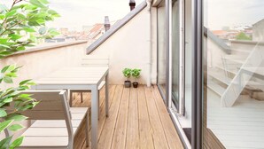 A wooden deck with a table and chairs, potted plants, and a glass door leading to a city view. - Stylish Terrace Apartment in Antwerp (Antwerp)