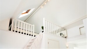 A white interior with a staircase leading to a loft area, a small window, and a door. - Stylish Terrace Apartment in Antwerp (Antwerp)