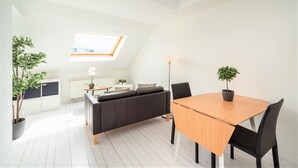 A modern, well-lit room with a skylight, a wooden dining table, black chairs, a dark sofa, and potted plants. - Stylish Terrace Apartment in Antwerp (Antwerp)