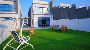 A modern building with a flat roof, a balcony with glass railings, and a well-maintained lawn with outdoor furniture. - Brand New Island Villa 4B+Pool Full sea view (Fujairah)