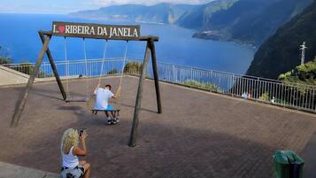 Eine Schaukel mit einem Schild, auf dem 'I ♥ RIBEIRA DA JANELA' steht, und im Hintergrund Meer und Berge.