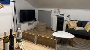 A modern living room with a flat-screen TV, a sofa, a coffee table, and a dining area with a table and chairs. - Holiday Home 'Palheiro Dis 3’as' with Sea View, Wi-Fi and Air Conditioning (Achadas da Cruz)
