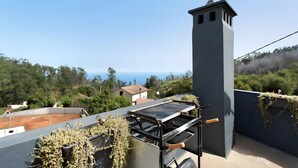 A rooftop terrace with a grill, a chimney, and a view of the sea. - Holiday Home 'Palheiro Dis 3’as' with Sea View, Wi-Fi and Air Conditioning (Achadas da Cruz)