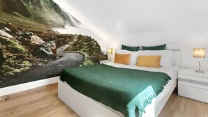 A bedroom with a bed, a nightstand, a lamp, and a wall mural of a mountainous landscape. - Holiday Home 'Palheiro Dis 3’as' with Sea View, Wi-Fi and Air Conditioning (Achadas da Cruz)