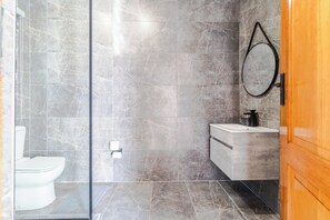 A modern bathroom with a glass shower enclosure, a toilet, a sink, and a wooden door. - Boutique Hotel-Style Room In Ferndale-G7 (Randburg)