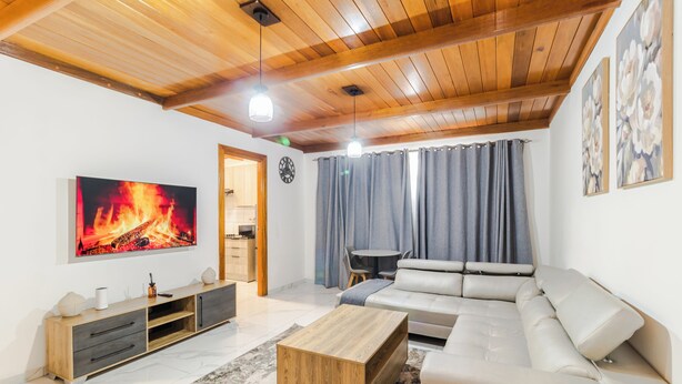 A modern living room with a wooden ceiling, a large TV, a sofa, a coffee table, and a fireplace. - Boutique Hotel-Style Room In Ferndale-G7 (Randburg)