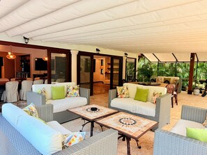 An outdoor patio area with wicker furniture, a dining table, and a TV in the background. - Tropical Luxury Villa in Casa de Campo with pool and beach access (La Romana)