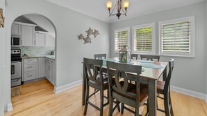 Una cocina con armarios blancos, una mesa de comedor de madera con sillas y una araña.