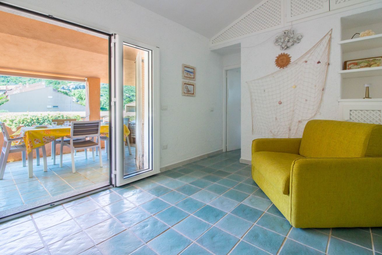 A room with a sliding glass door leading to an outdoor area, a yellow sofa, and a tiled floor.