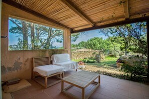 A covered outdoor seating area with a bench and a table, a stone wall, and a view of trees and greenery. - Charming 51m2 apartment, located on the ground floor of a modern residential complex, capable of hosting up to 4 people.Located just 6 minutes by car from Palau, one of the pearls in Northern Sardinia, the property is located in a context that combines n (Pulcheddu)