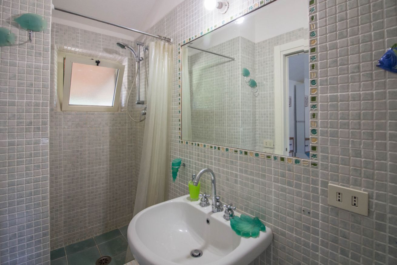 A bathroom with a sink, mirror, shower, and tiled walls.