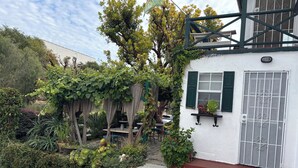 Un edificio blanco con contraventanas verdes, una reja de metal y un jardín con diversas plantas.