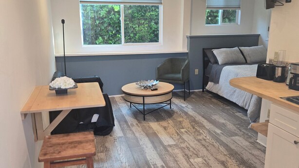 Habitación pequeña con cama, una mesa de comedor, un taburete, una mesita redonda y un ventilador de techo.