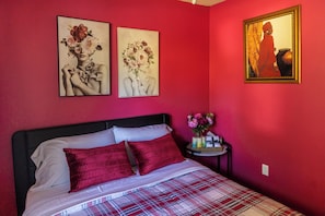 Um quarto com cama, almofadas, mesa de cabeceira e decoração na parede.