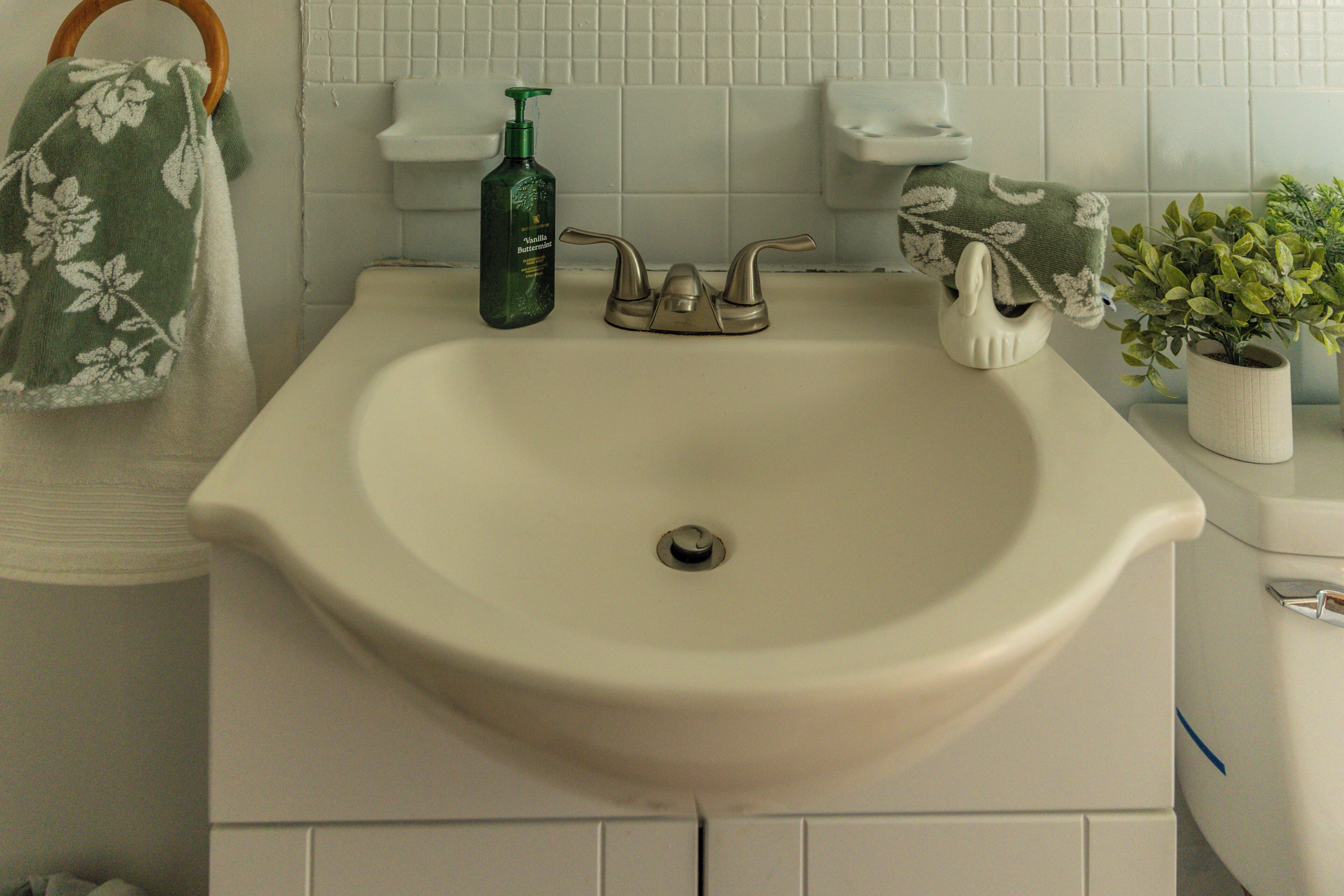 A bathroom sink with a green bottle, a towel, and a potted plant.